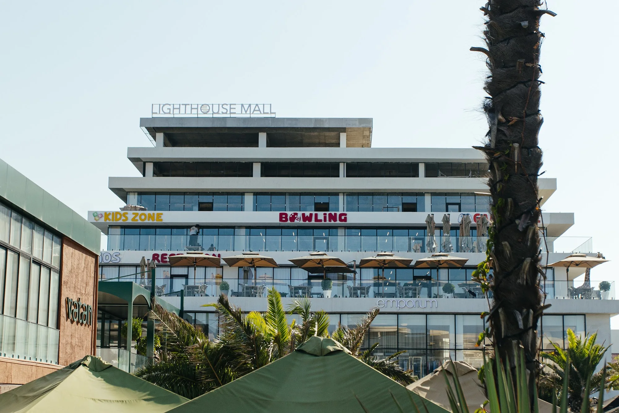 Lighthouse Mall: на верхнем ярусе вывески KIDS ZONE и BOWLING, ниже терраса с зонтами, внизу — Emporium